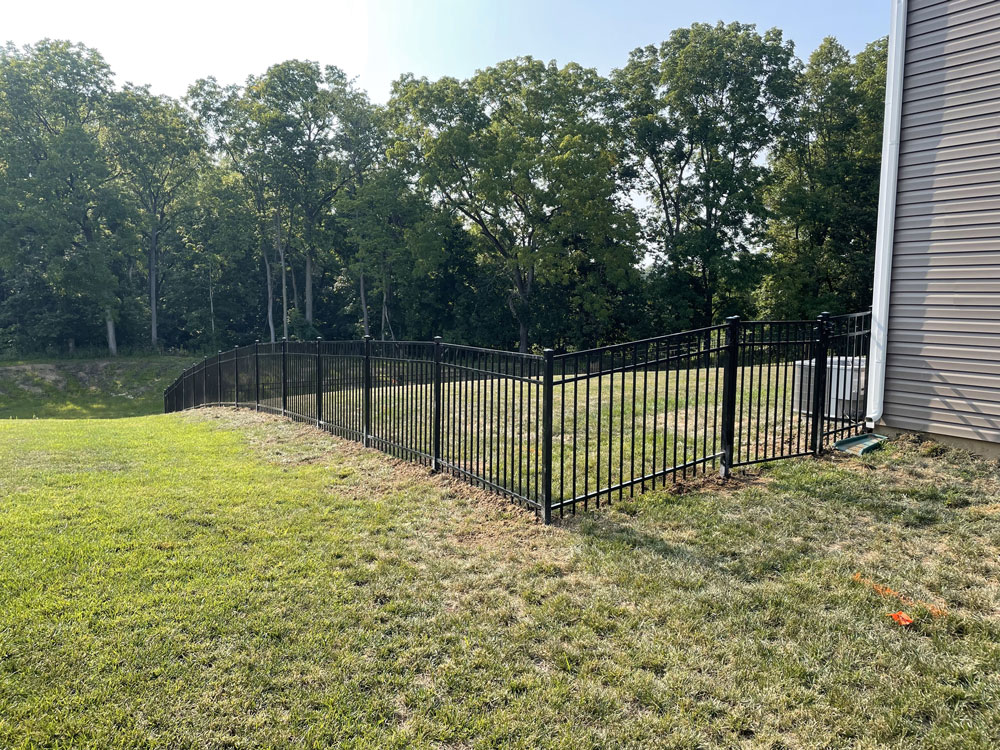 A black aluminum fence with gate closes off a backyard in an L-shape and slopes down a hillside.
