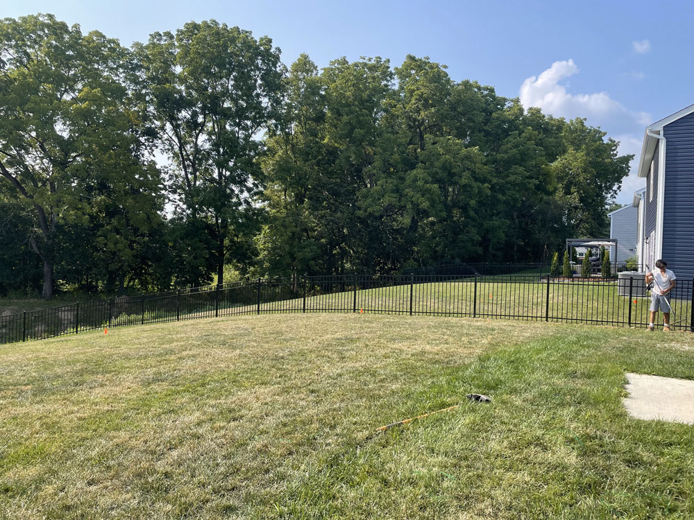 Black aluminum fences close off the backyard of two houses and tall trees stand in the background.