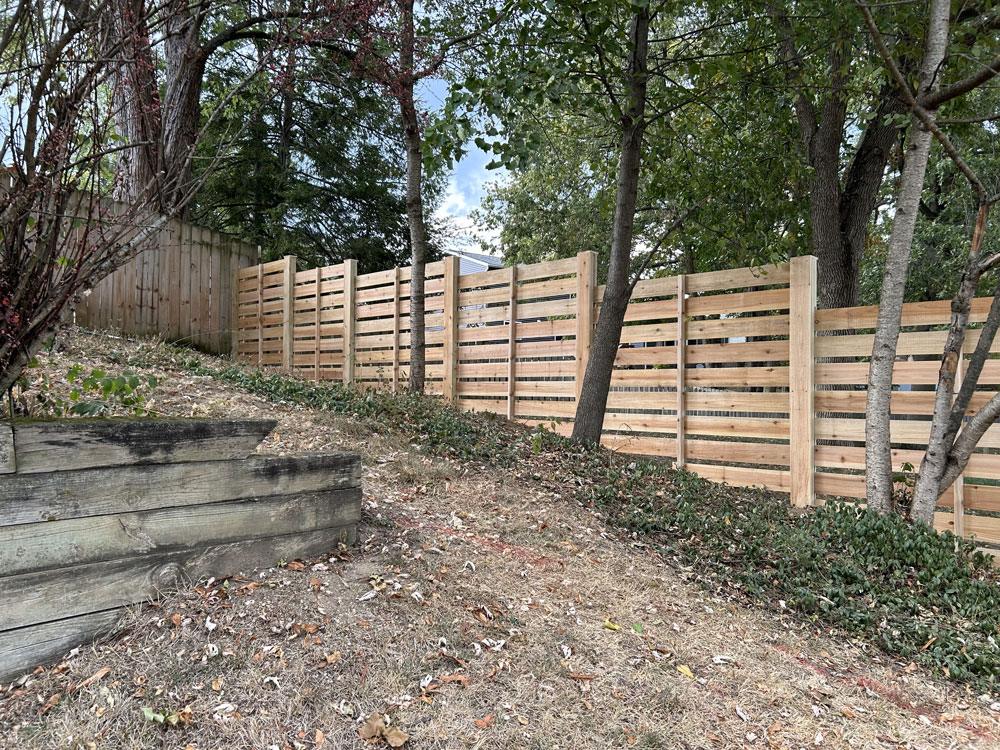A custom wood stepped height fence going down a sloped hill.