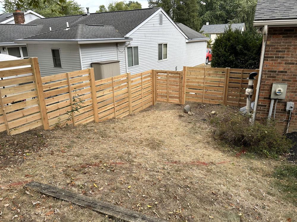 A custom wood stepped height fence going down a sloped hill and curving at a right angle toward the side of a house.