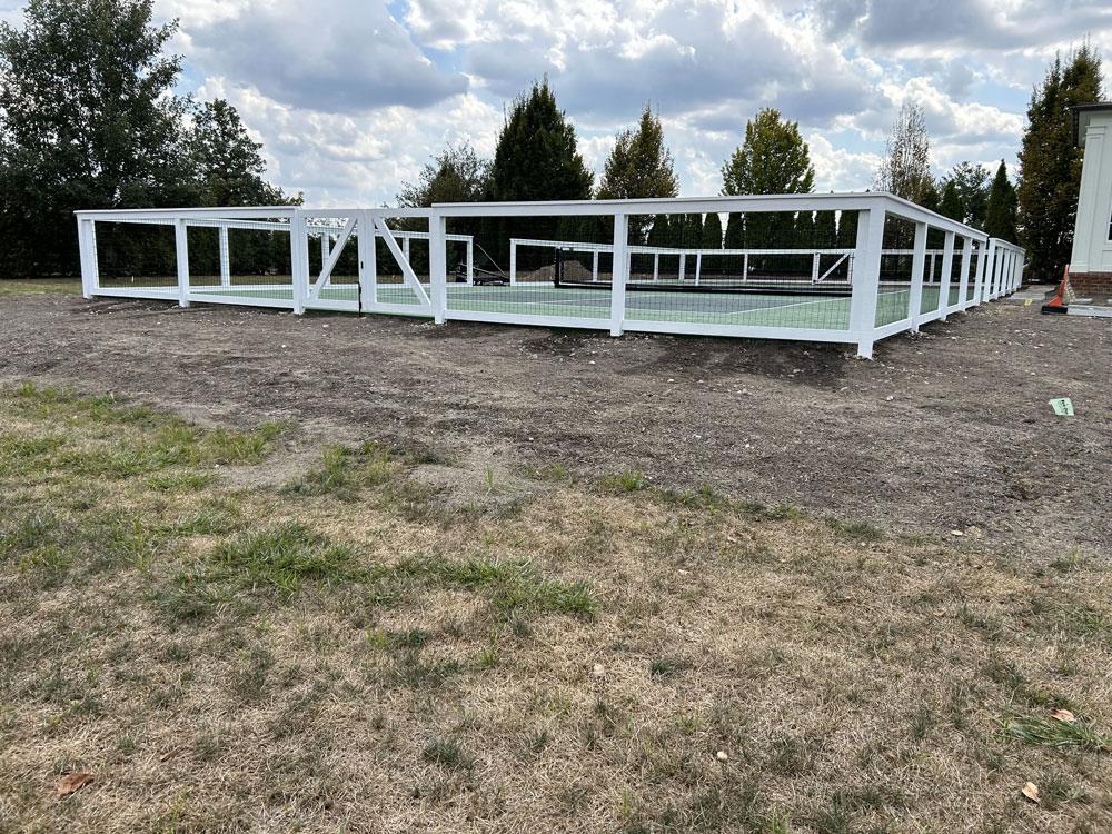 A custom white and wire tennis court fence with a gate.
