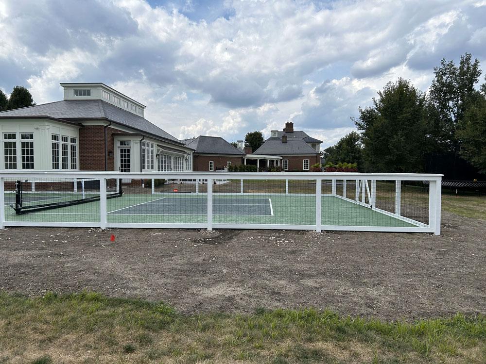 A custom white tennis court fence with wire and houses in the background.