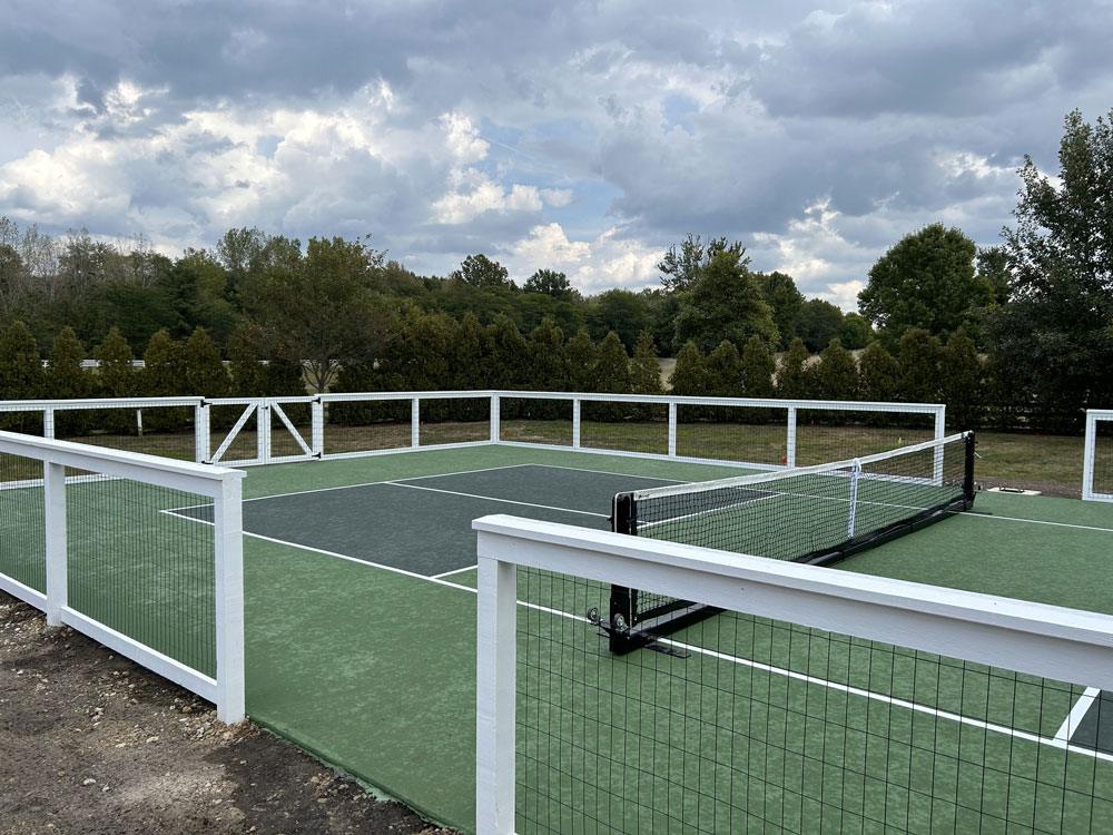 A closeup of the custom wire tennis court fence with a double gate in the background, and two open segments on either side.