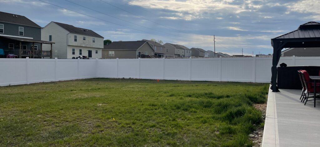 A white vinyl fence encloses a backyard with a long row of houses on the other side.