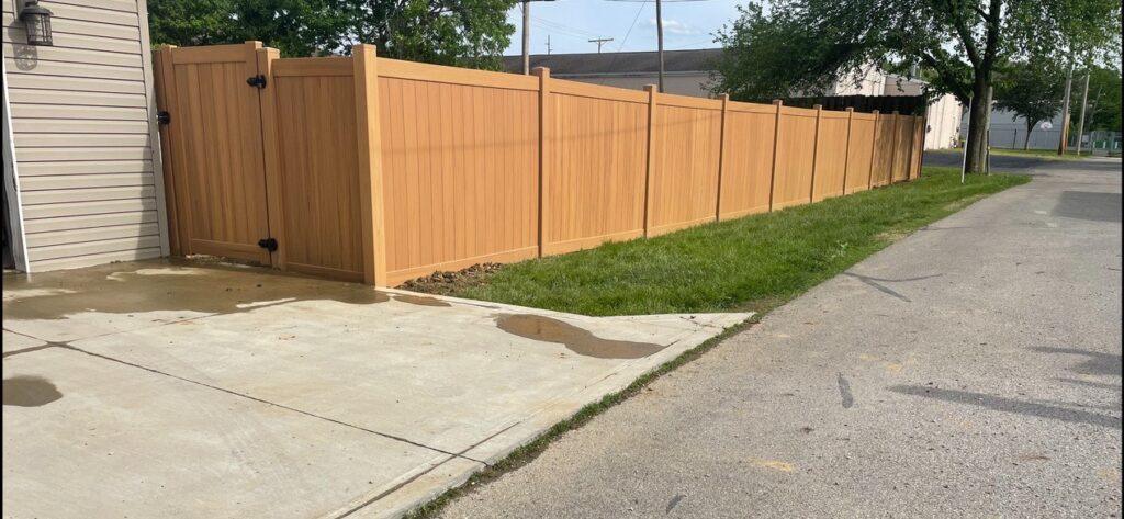 A brown vinyl fence with side gate separates a road from a home property.