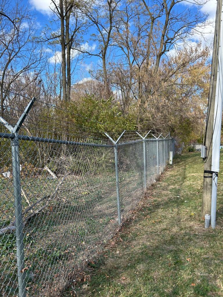 A commercial chain link fence with barbed wire on top separates two property lines.