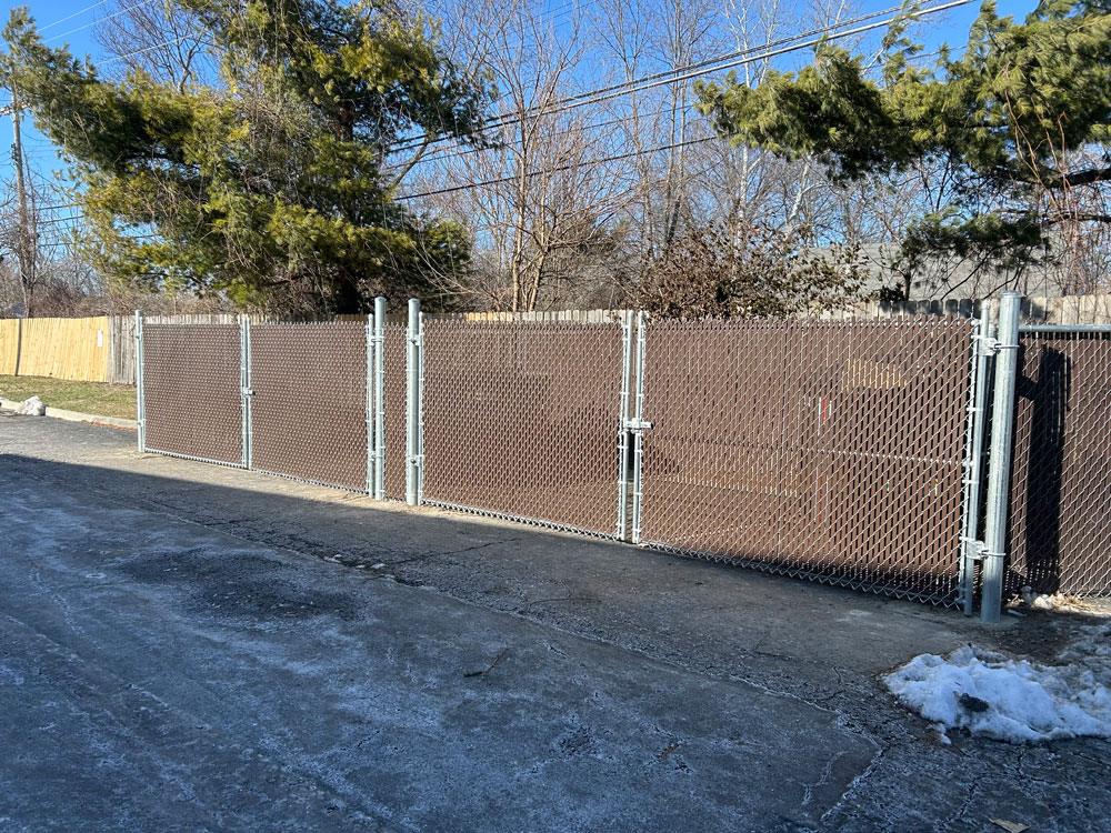A commercial chain link fence with privacy slats protects dumpsters from illegal trash disposal.