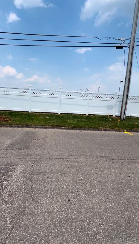 A commercial white vinyl fence installed near a parking lot.