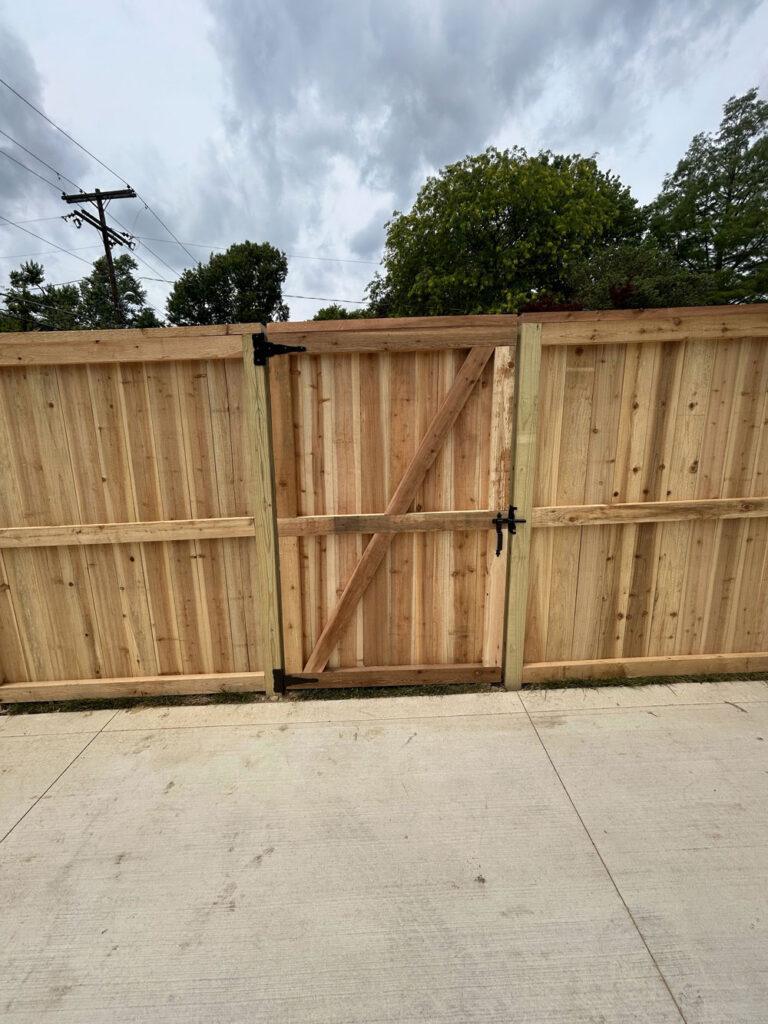 A wooden fence with a closed gate and black gate latch.