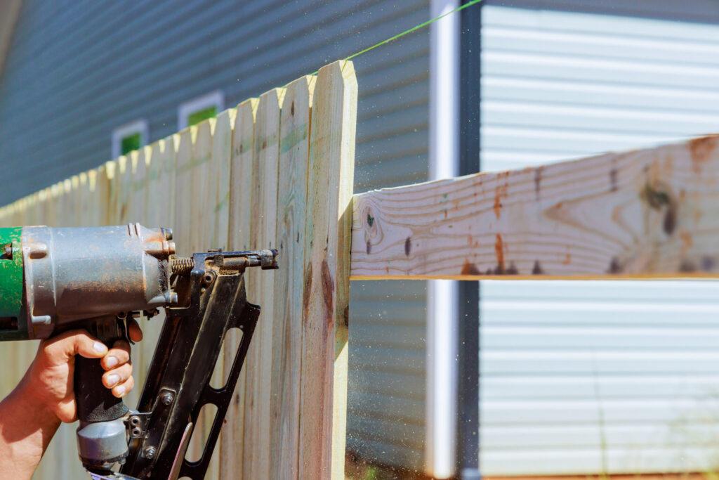 Man builds sections of nailing a wooden fence around his yard out planks
