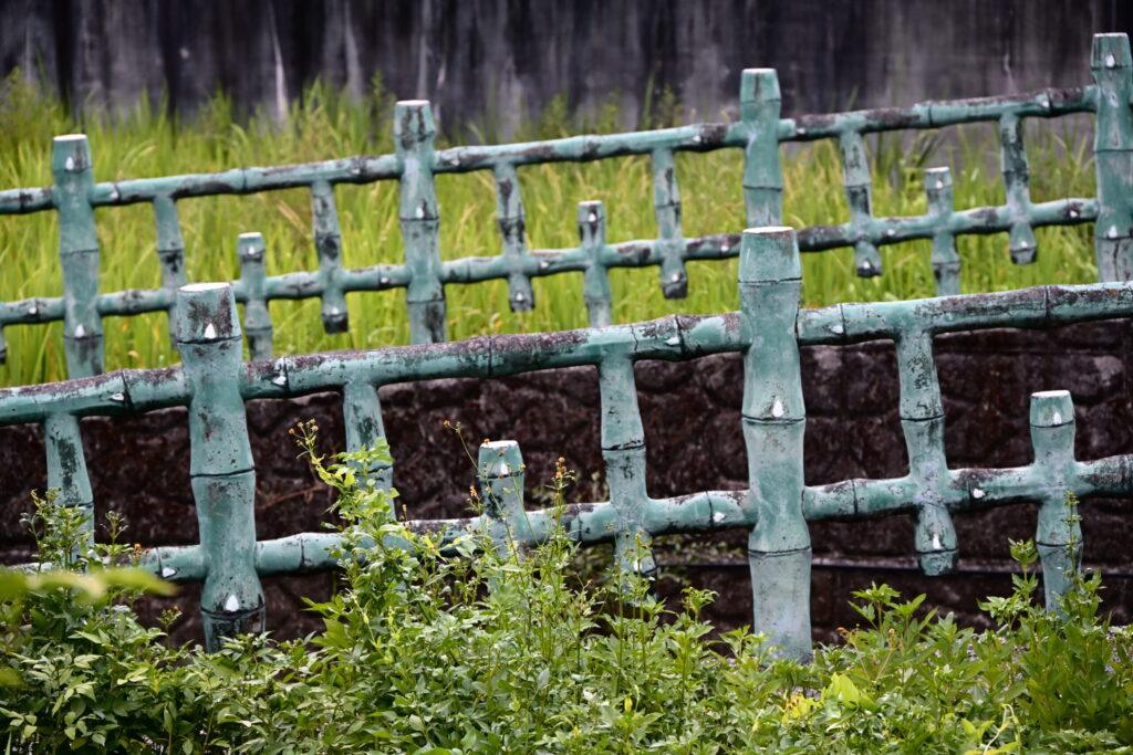 Green Bamboo-Style Fence with Weathered Patina Surrounded by Lush Garden Vegetation