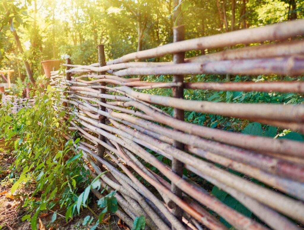 A rustic woven wooden fence stretches through a lush garden, surrounded by vibrant greenery.