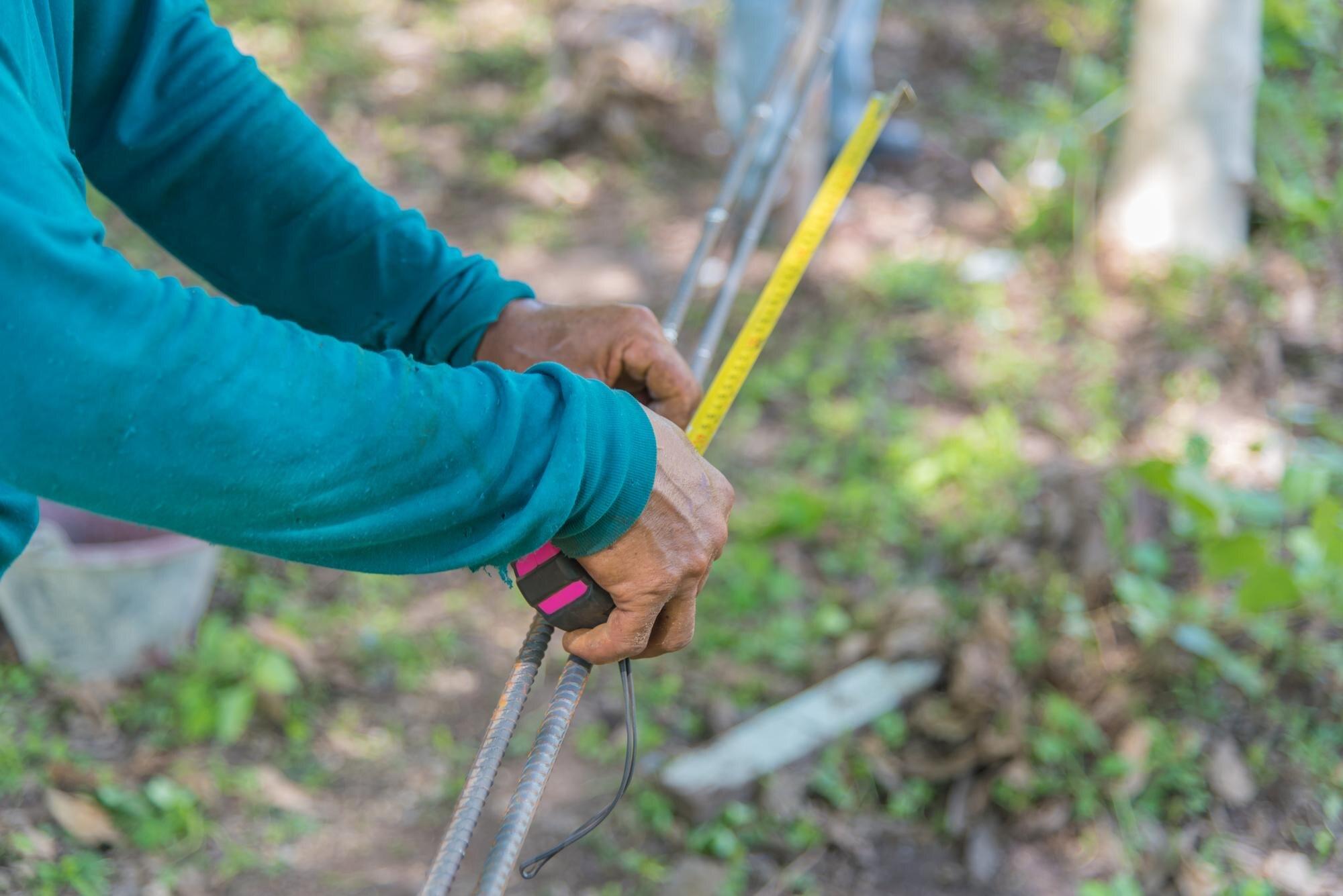 Cropped Hands Of Worker Measuring Metal Rod Over F